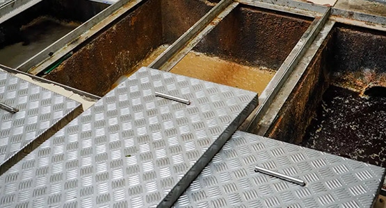 Restaurant grease trap with open lids showing interior compartments.