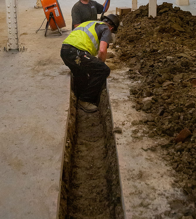 Construction workers digging a trench indoors.