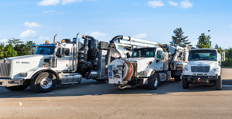 Street maintenance trucks parked outdoors in a row under a clear blue sky.
