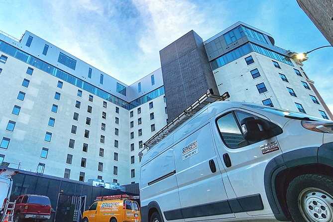 White service van parked beside a tall modern building under a blue sky.