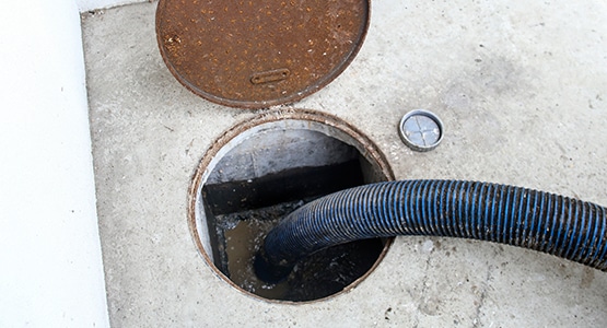 Hose inserted into a circular drain on cement, with rusty metal cover beside.