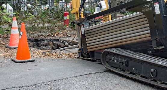 A horizontal directional drilling machine on a road near orange traffic cones.
