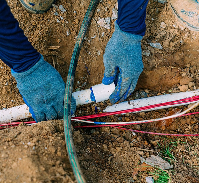 Person fixing underground pipes with blue gloves in dirt.