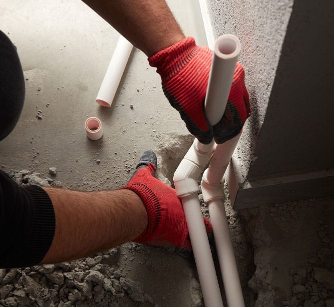 Person installing PVC pipes with red gloves in a construction site.