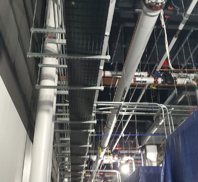 Industrial ceiling with pipes and cables in a large building under construction.