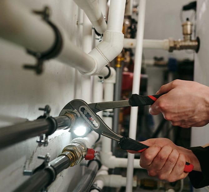 Person using pliers to fix pipes under bright light.