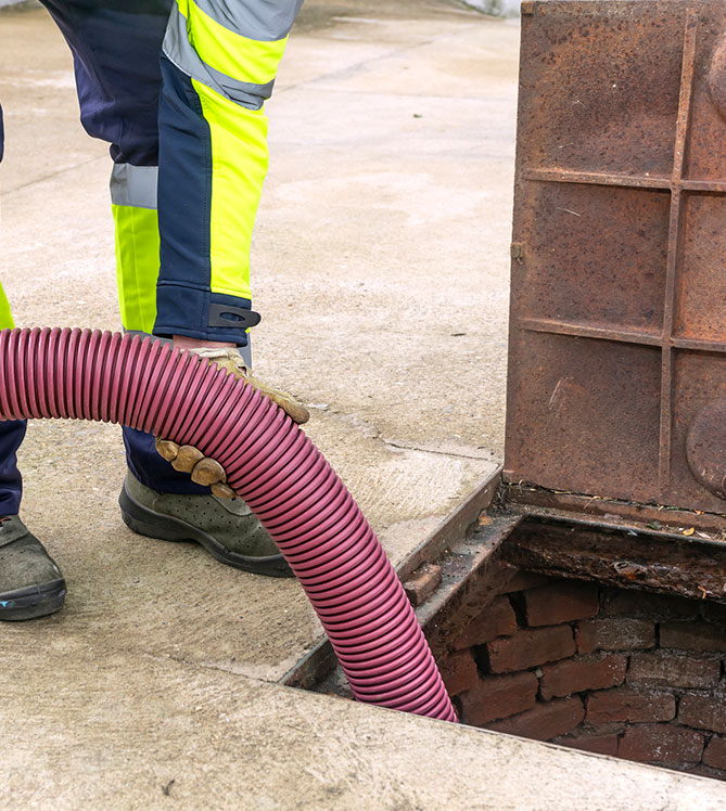 Worker in high-visibility gear using hose to clean a manhole.