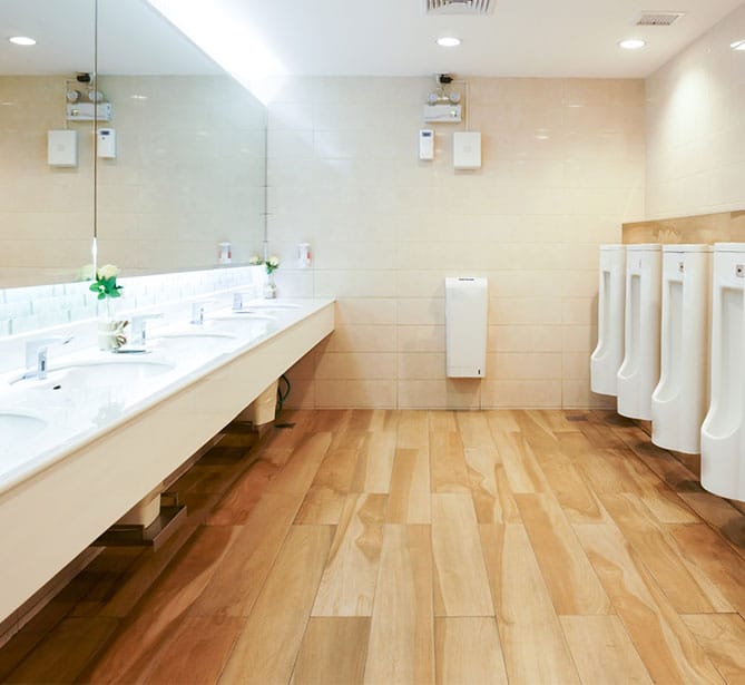 Modern public restroom with wooden flooring, sinks, mirrors, and urinals.