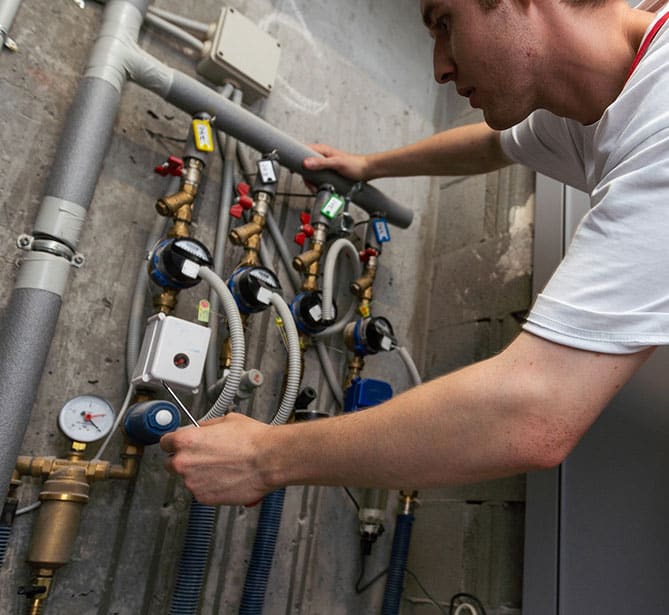 A person adjusting water valves and meters in a utility room.