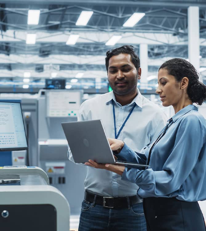 Two professionals discussing data on a laptop in a modern industrial facility.