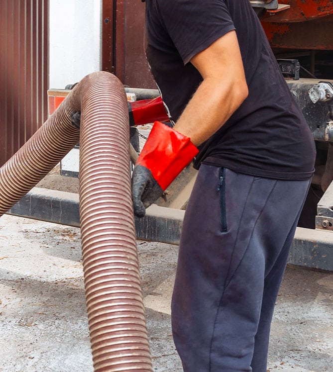 Person wearing red gloves handling large industrial hose outdoors.