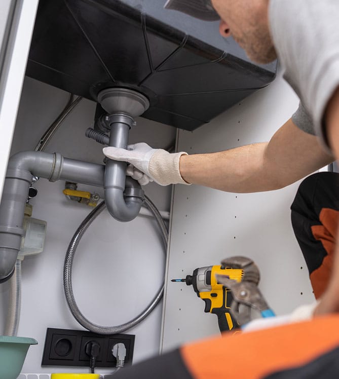 A plumber fixing pipes under a sink with tools on standby.