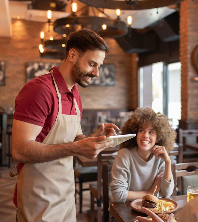 A waiter taking an order from a smiling woman in a cozy restaurant setting.