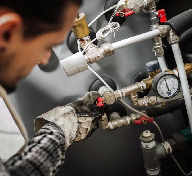 Person adjusting valves on industrial equipment with gauges.
